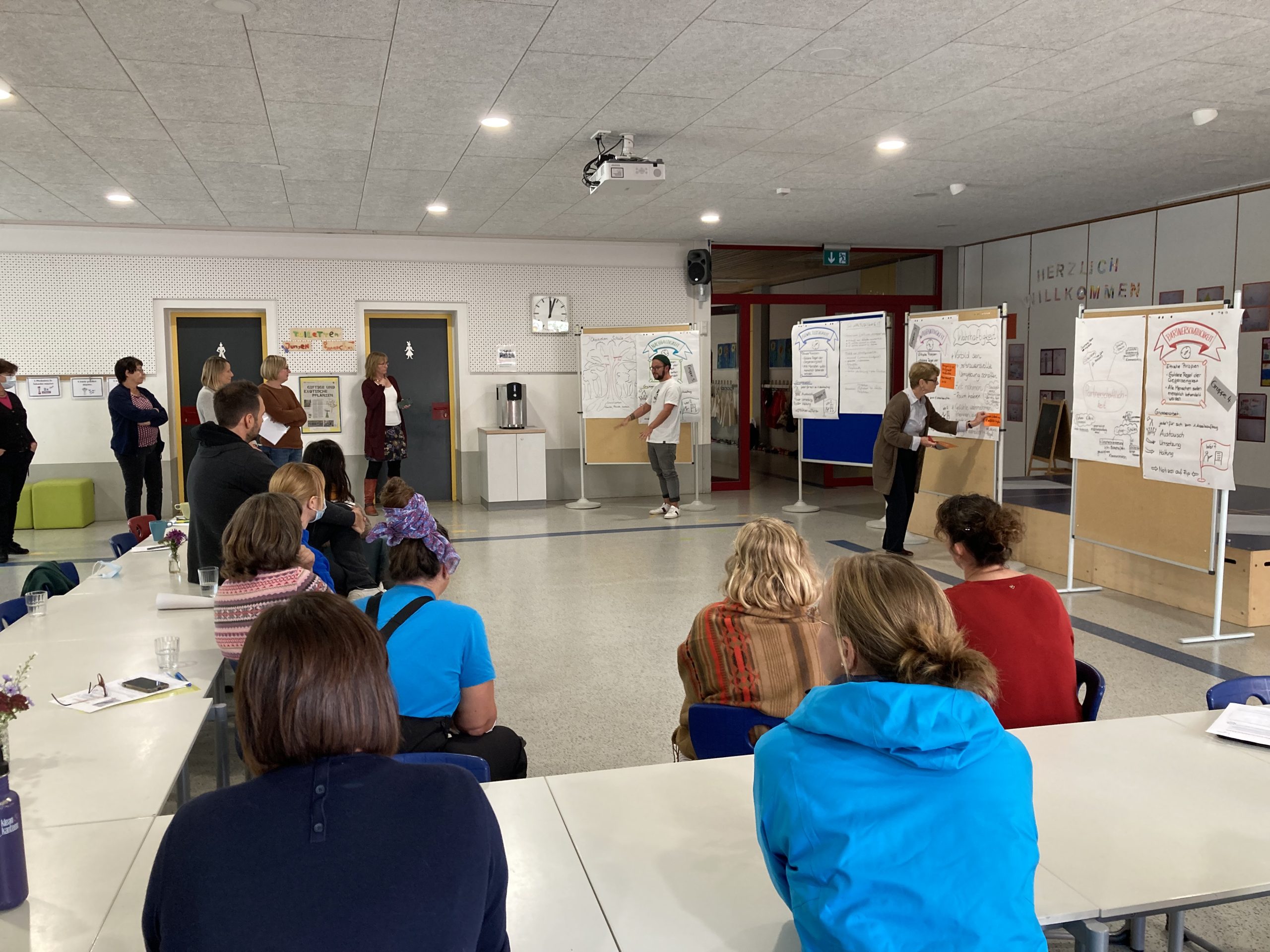 Das Bild zeigt Schüler*innen und Lehrer*innen vor Pinnwänden mit selbstgemachten Plakaten bei einem Workshop beim Pädagogischen Tag der Weltethos Stiftung.