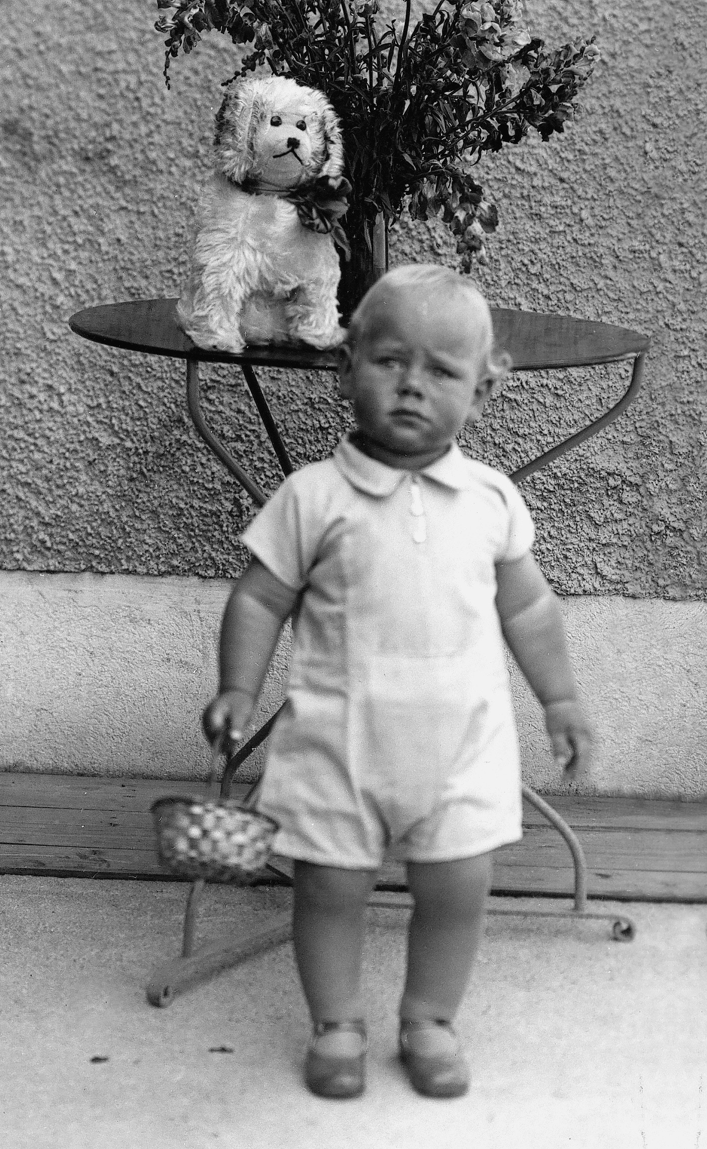 Das Bild ist schwarz-weiß und zeigt den Gründer der Weltethos Stiftung Hans Küng als Kleinkind stehend vor einem Gartentisch.