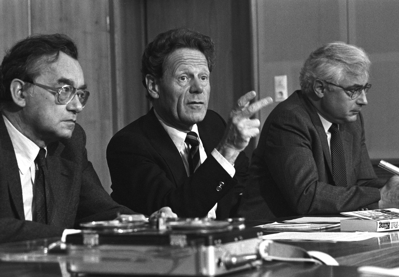 Das schwarz-weiße Bild zeigt Hans Küng gestikulierend an einem Tisch bei einer Pressekonferenz.