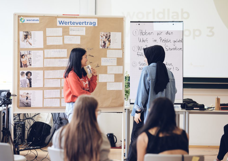 Das Foto zeigt Schüler*innen vor einer Flipchart im Klassenzimmer während eines worldlab Workshop für Demokratiekompetenz.