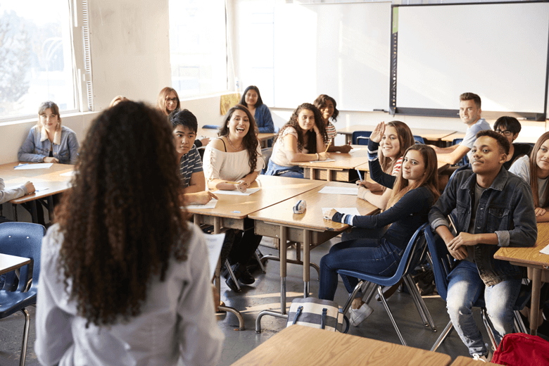 Symbolbild für Weltethos in der Schule: Mädchen im Teenager-Alter steht in Klassenzimmer und hält Weltethos Unterrichtsmaterial