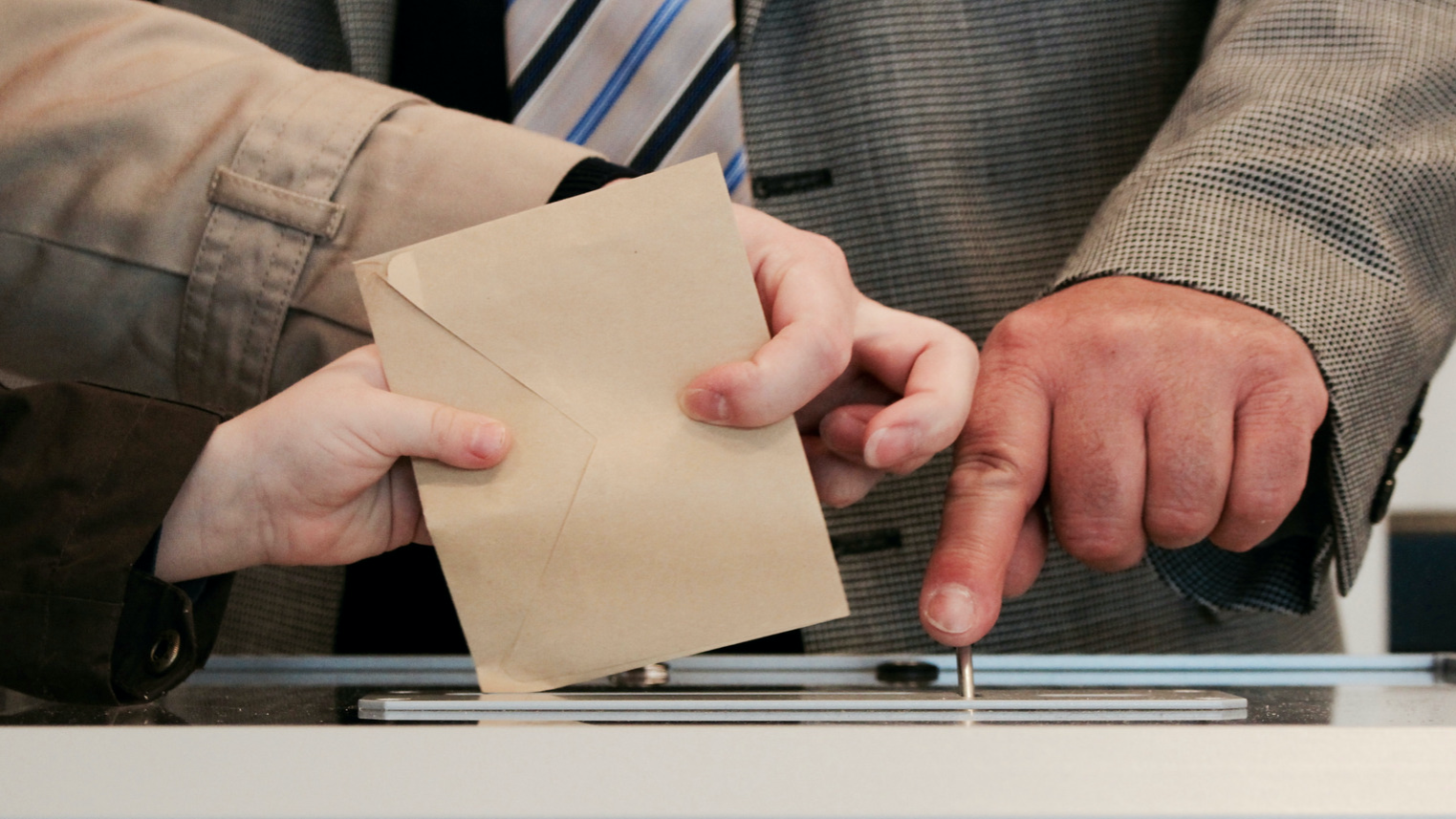 Ein Brief wird in eine Wahlurne geworfen als Zeichen für Demokratie