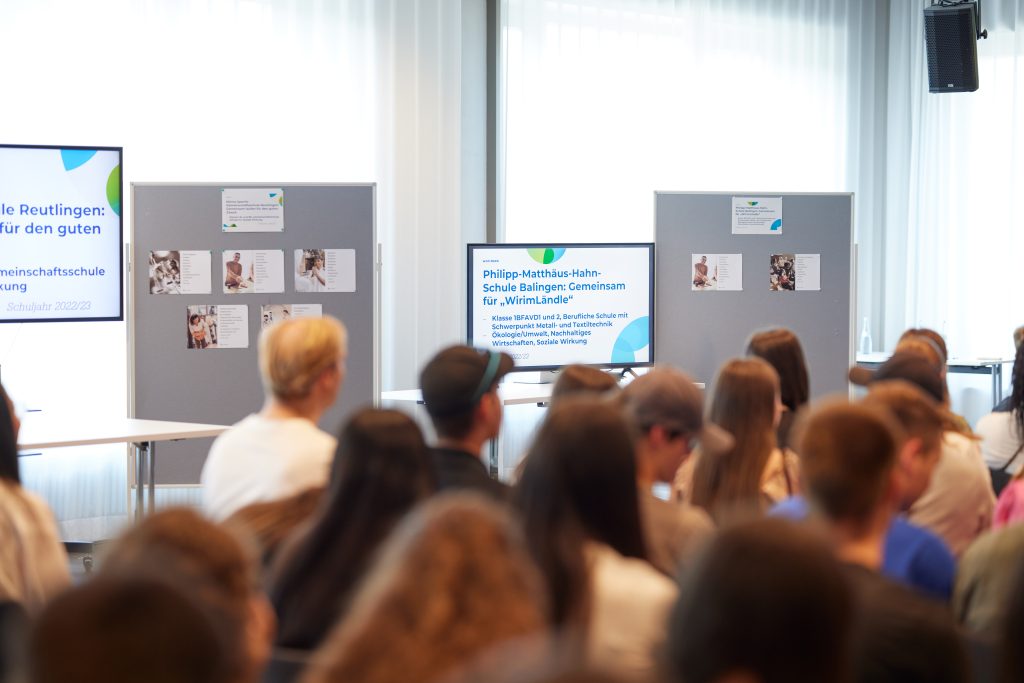 Das Publikum ist von hinten zu sehen, dahinter steht ein Bildschirm, auf dem eine Präsentation das Projekt der Philipp-Matthäus-Hahn-Schule aus Balingen zeigt.