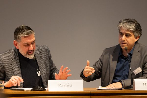 Zwei Männer sitzen vor Mikrofonen und diskutieren miteinander.