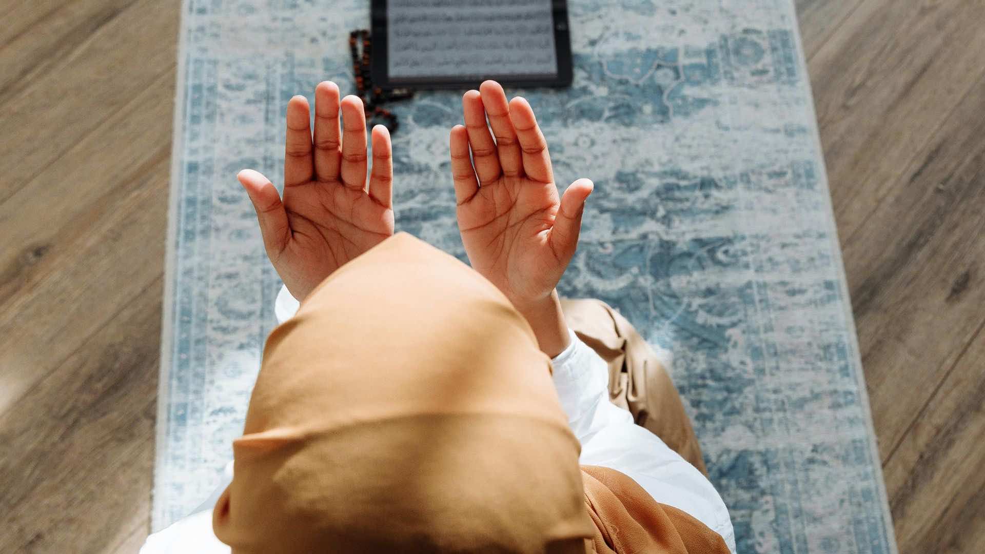 Eine Frau islamischen Glaubens sitzt auf einem Gebetsteppich und betet.