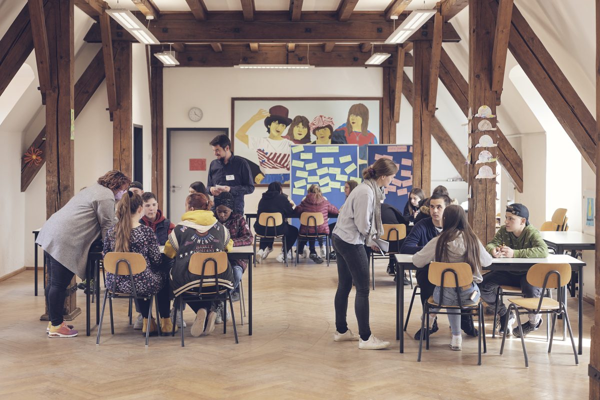 Das Foto zeigt Schüler*innen an Gruppentischen im Klassenzimmer verteilt während eines worldlab Workshop für Demokratiekompetenz.
