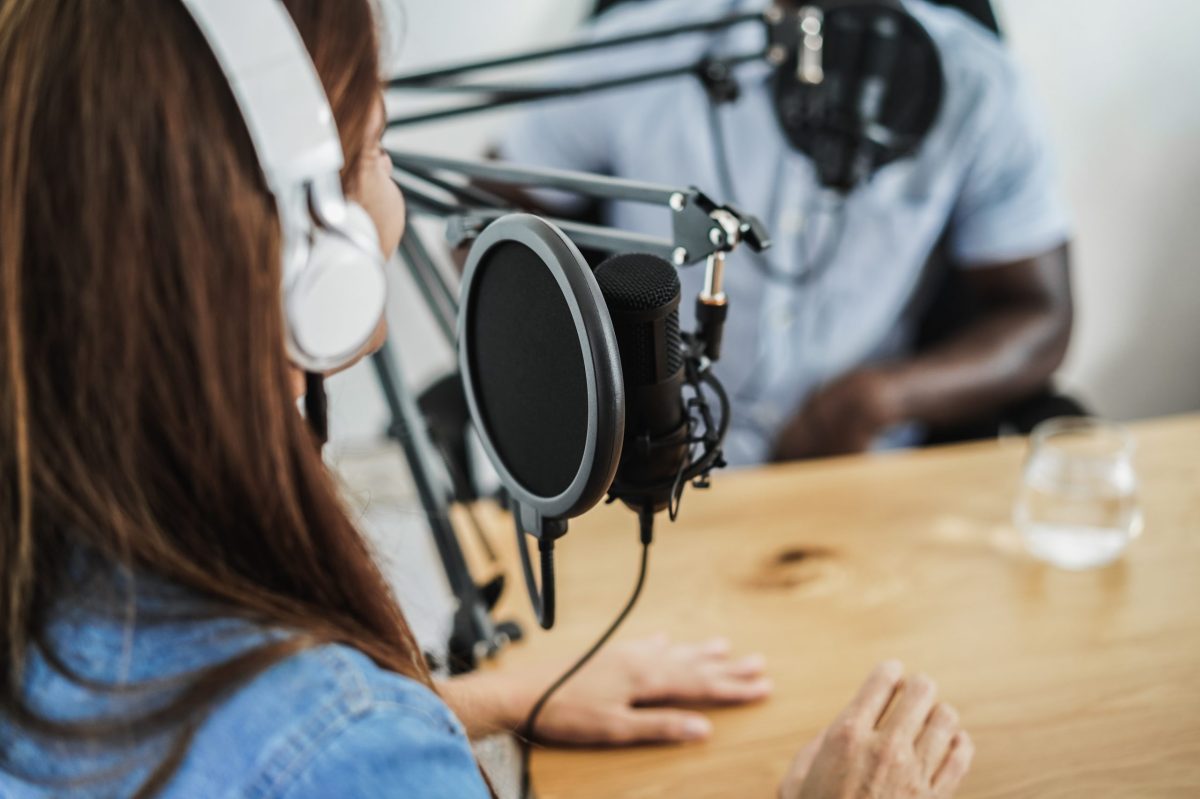 Multirassische Gastgeber führen ein Interview, während sie gemeinsam im Heimstudio einen Podcast streamen - Fokus auf das Mikrofon