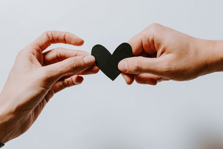 Das Bild zeigt zwei Hände, die ein schwarzes Herz aus Papier halten.