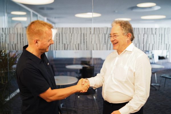 Das Bild zeigt den Gründungsdirektor des Weltethos Insitut Prof. Claus Dierksmeier und seinen Nachfolger Prof. Ulrich Hemel, die sich lachend die Hand schütteln.