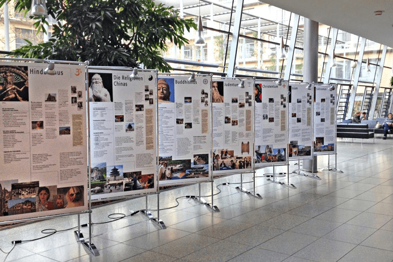 Das Bild zeigt acht große Informationstafeln aufgestellt nebeneinander in einem Foyer als Weltethos Ausstellung.